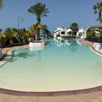 Fotografia de Piscina con palmeras en los alrededores y un edificio de dos plantas de fondo color blanco pintado con pintura para exteriores